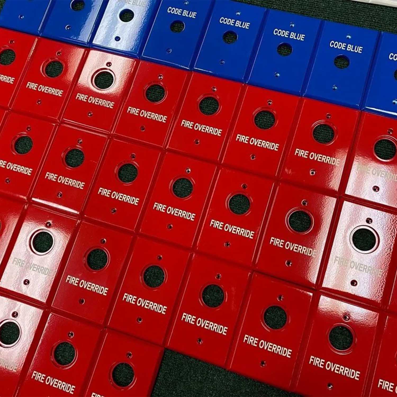 Blocs rouges et bleus accolés, imprimés “FIRE OVERRIDE” et “CODE BLUE” sur des casiers, girantes visées rondes noires. Blocs rouges et bleus accolés, imprimés “FIRE OVERRIDE” et “CODE BLUE” sur des casiers, girantes visées rondes noires.